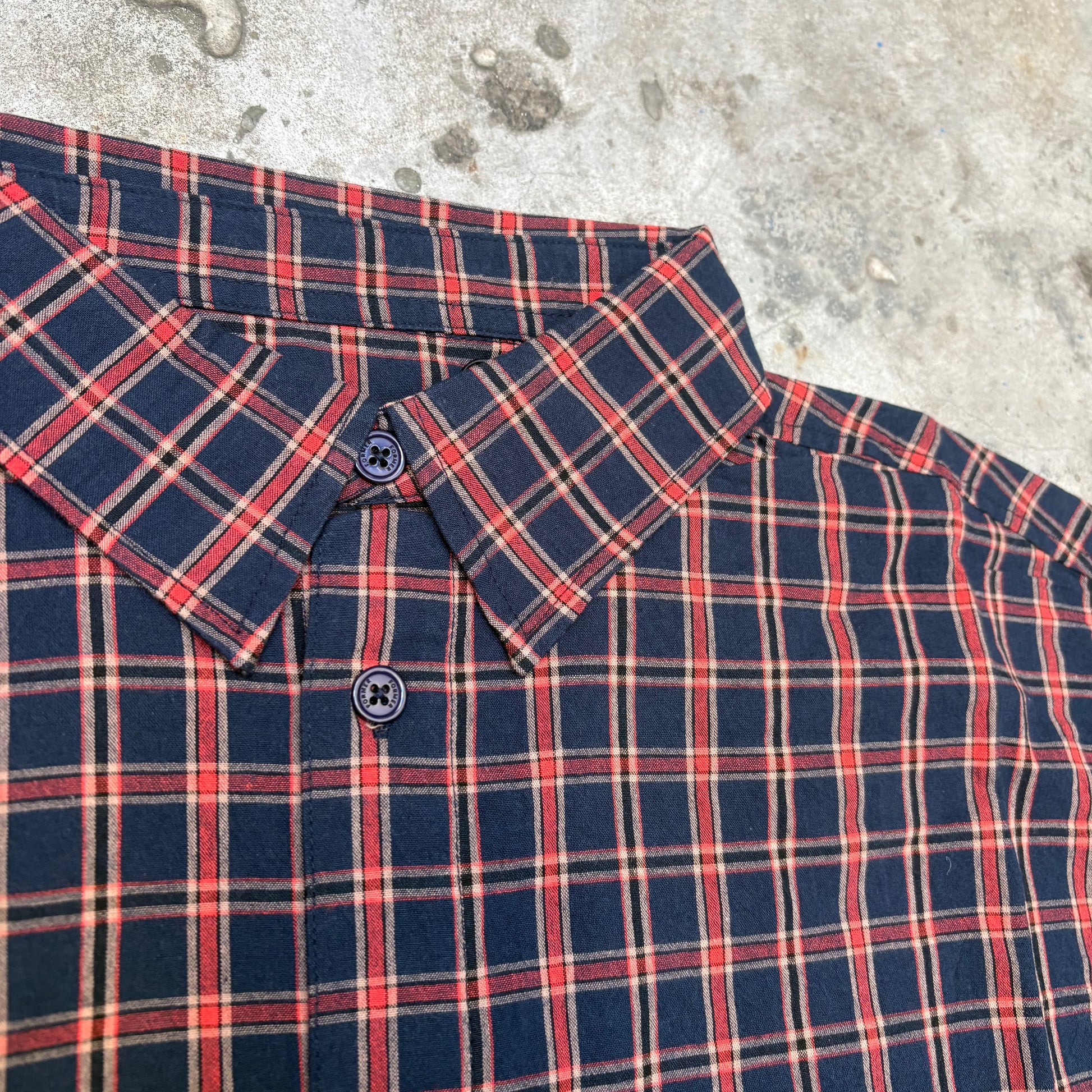 Close-up of a navy and red plaid shirt on a concrete surface