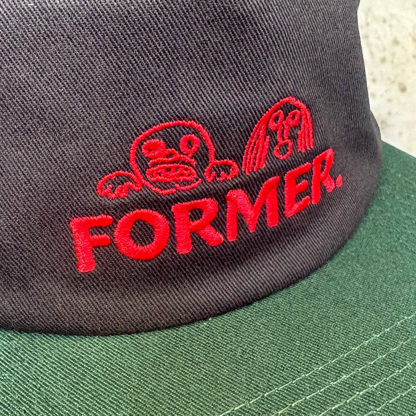 Green and black cap with red 'FORMER' logo on a textured surface