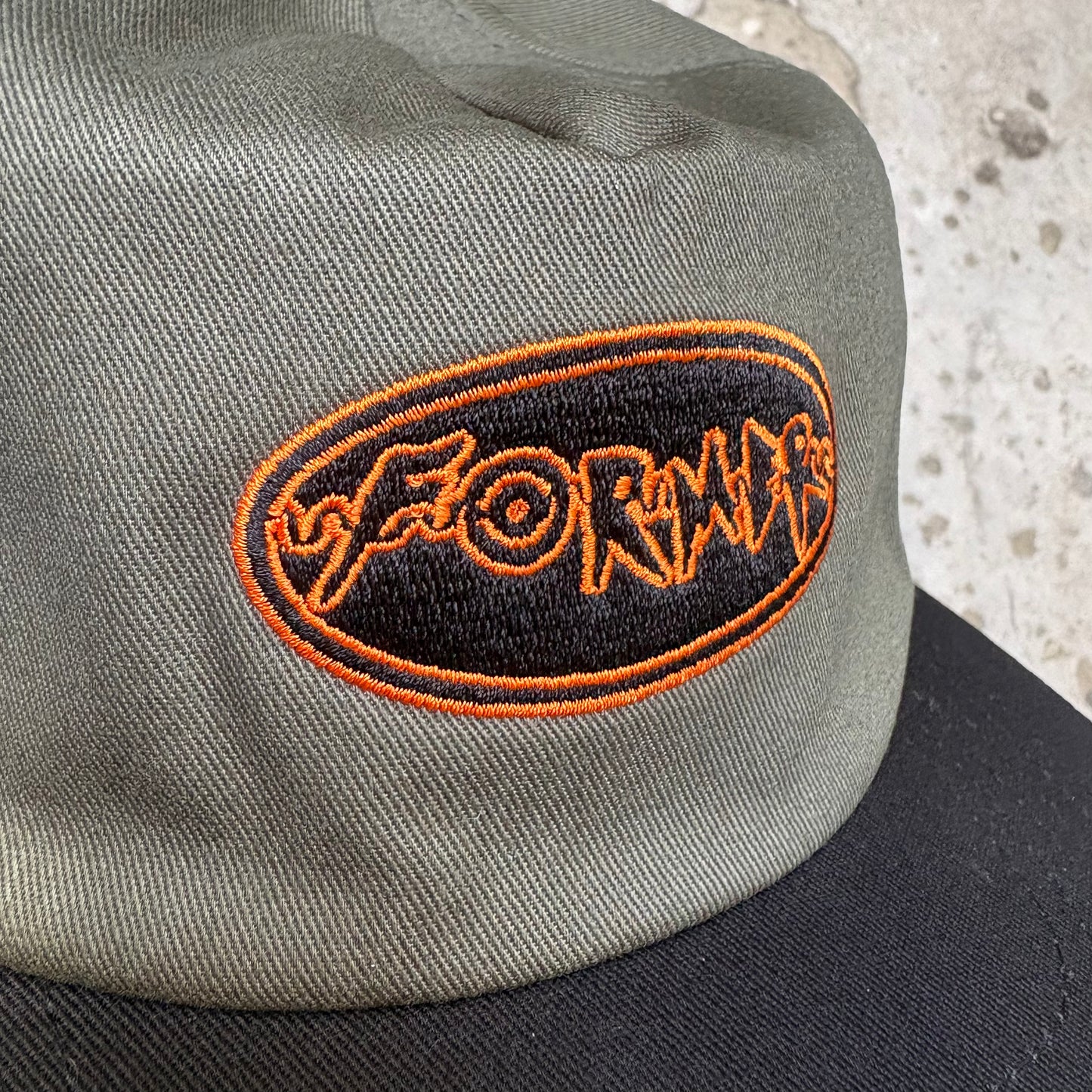 Gray cap with orange and black embroidered logo on a textured surface