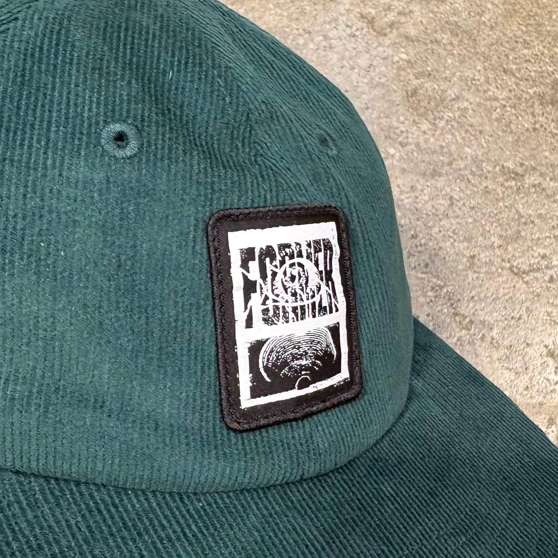 Green Former cap with a black and white patch on a concrete surface