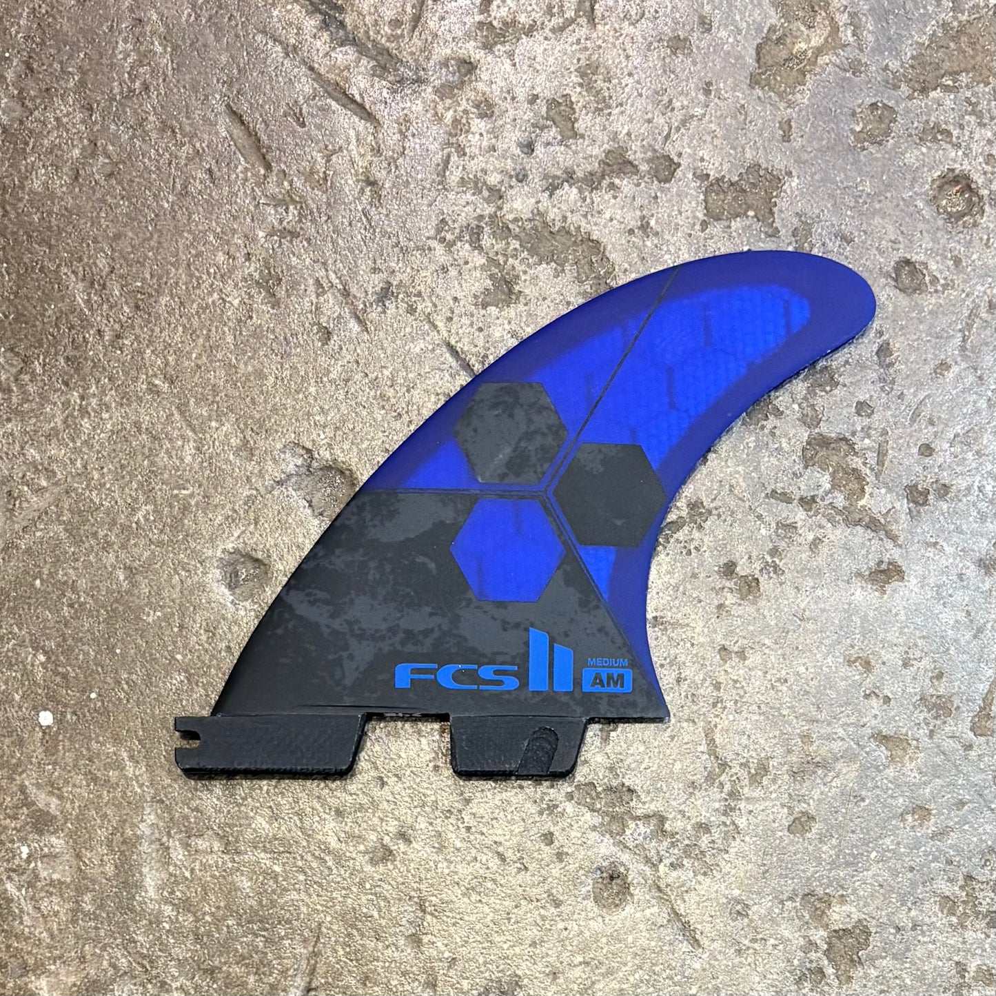 Blue and black FCS surfboard fin on a textured surface
