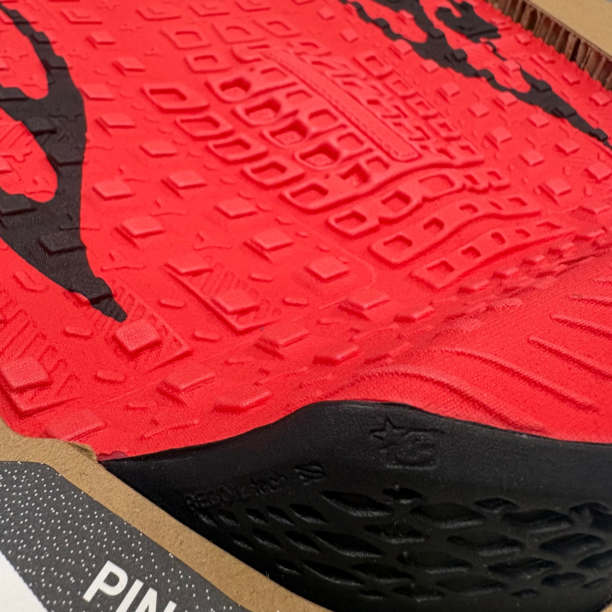 Close-up of a red and black athletic shoe sole with brand logo.