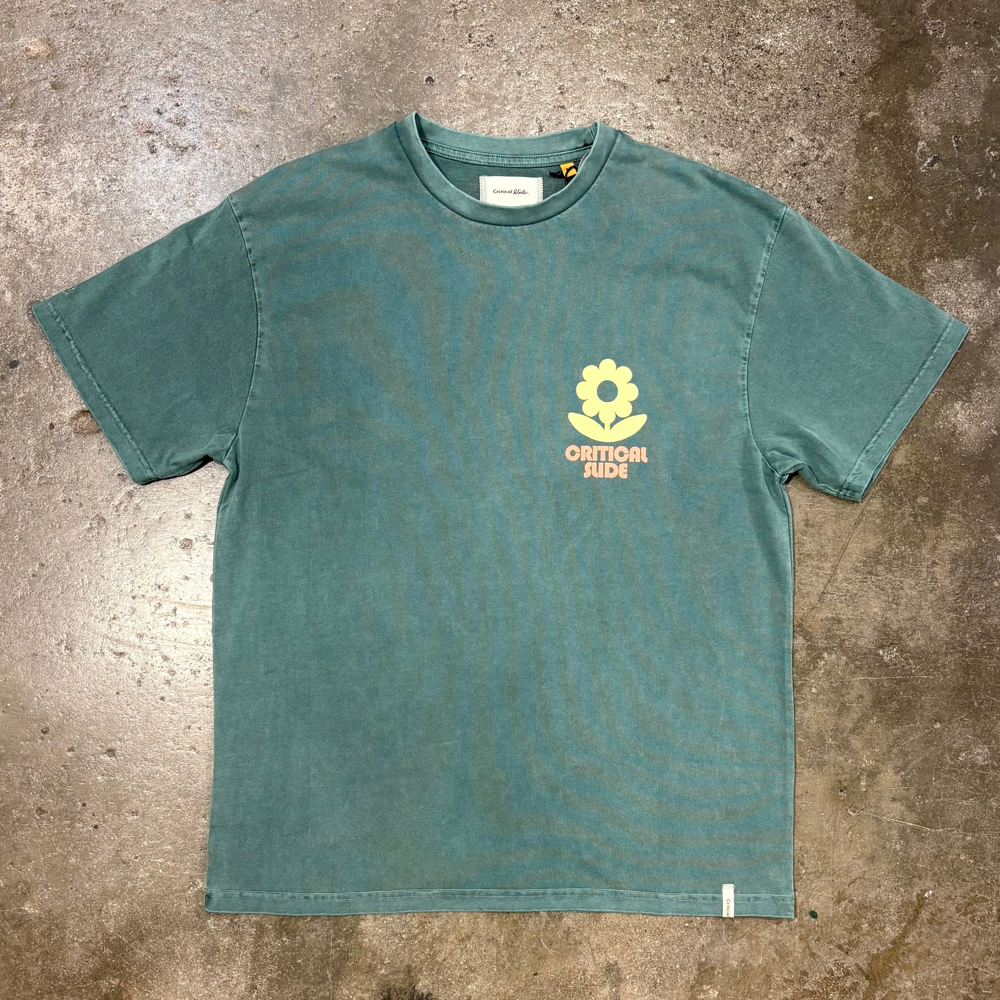 Green t-shirt with a yellow flower logo on a textured surface
