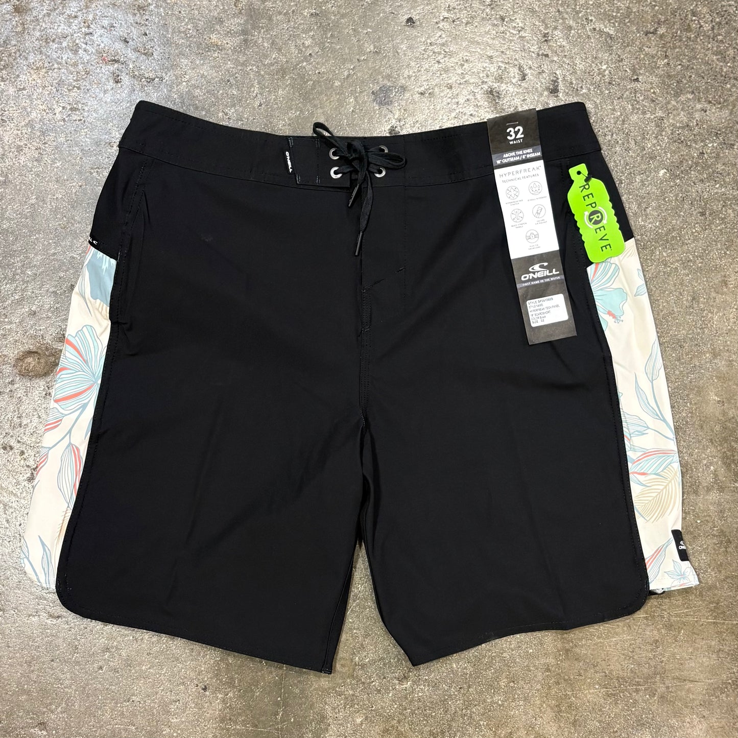 Black board shorts with floral side panels on a concrete surface