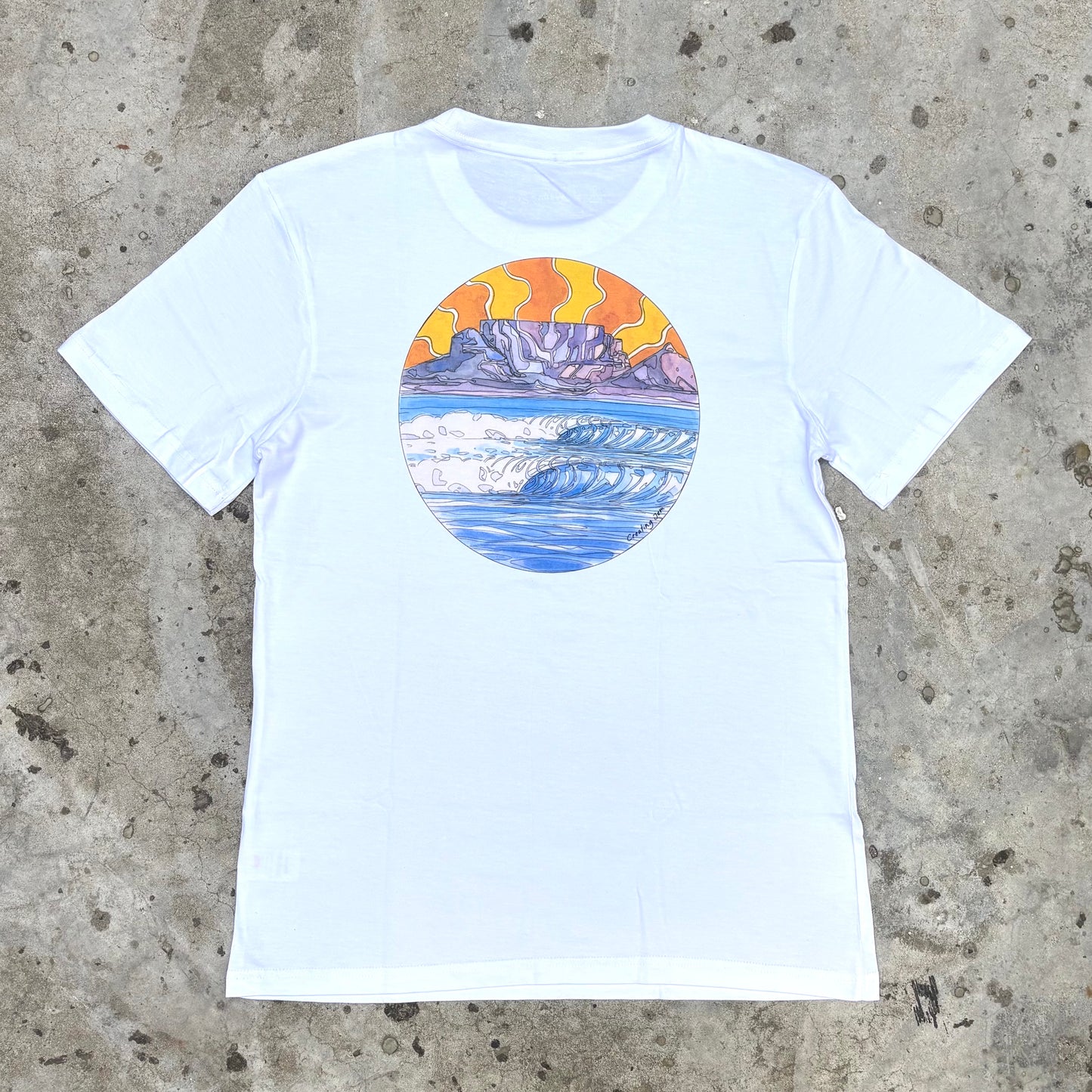 White t-shirt with a colorful graphic of a mountain and sunset on a concrete surface