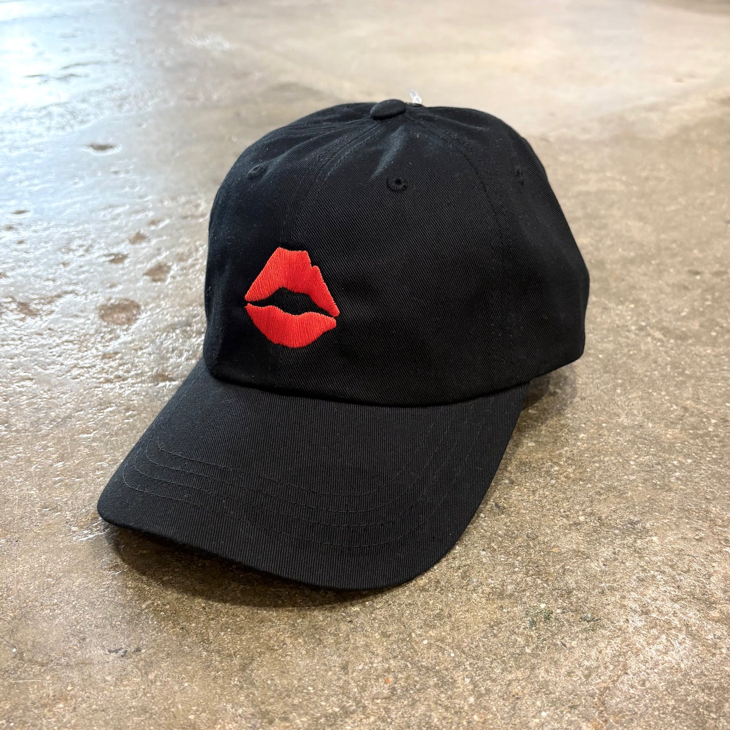 Black KISS Dad Cap with red Lips embroidery on concrete floor