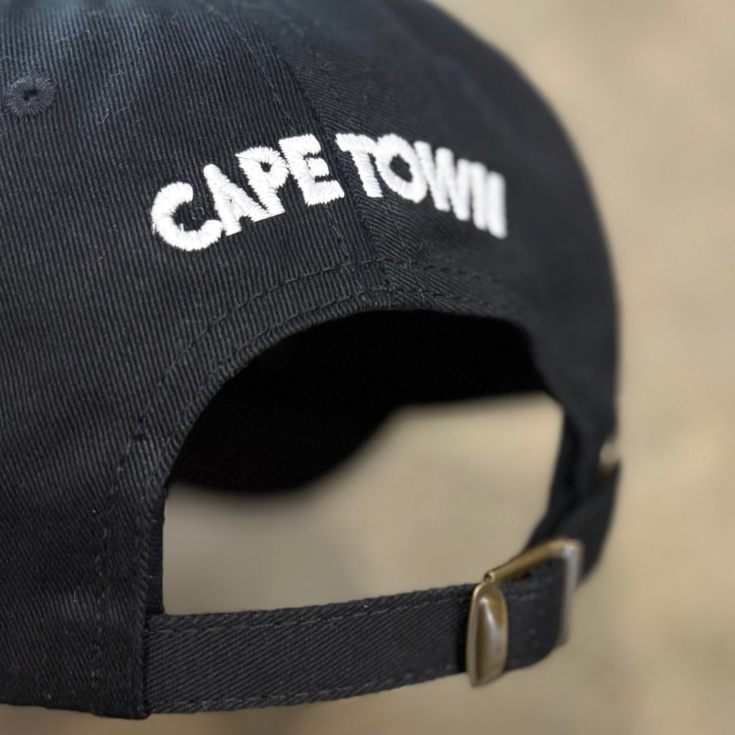 Black cap with 'Cape Town' embroidered on the back against a blurred background