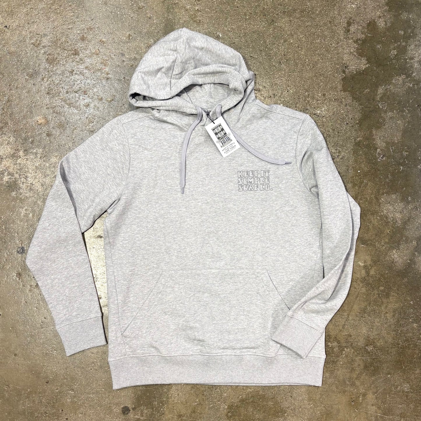 Gray 'Keep it simple surf' hoodie with a tag on a concrete surface