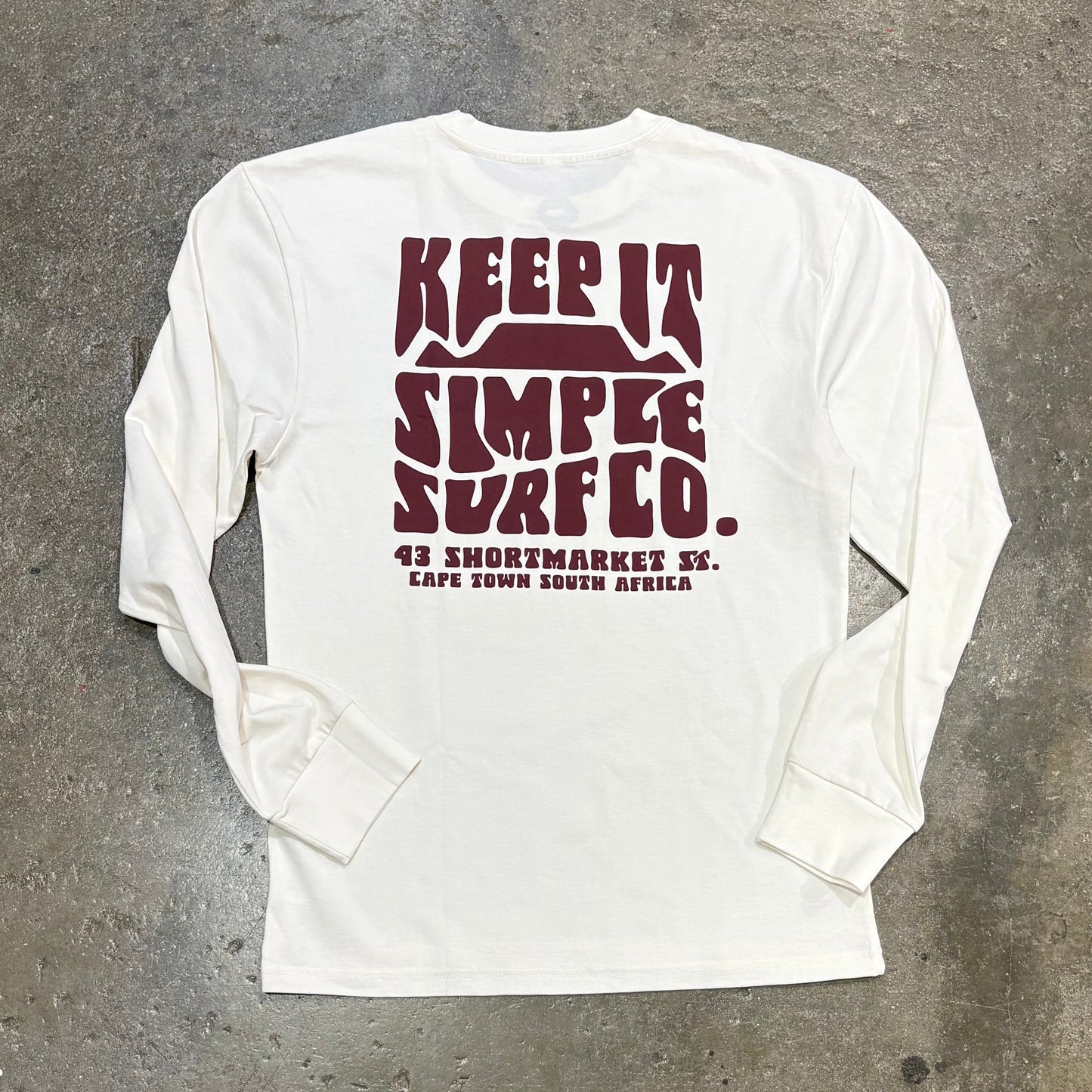 White long-sleeve shirt with maroon text on a gray concrete surface