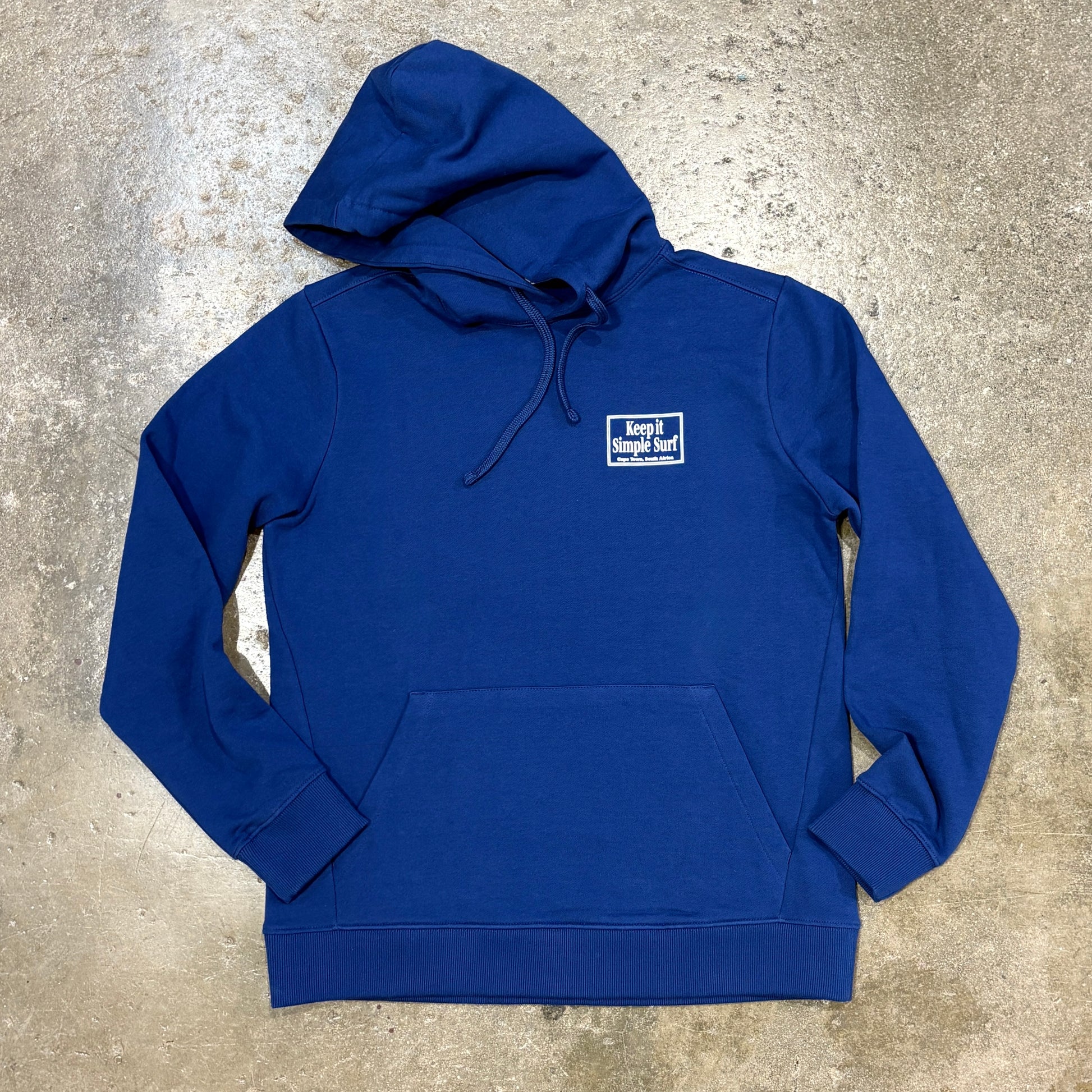A royal blue pullover hoodie with a small white embroidered 'keep it local' logo on the left chest, laid flat on a textured concrete surface.