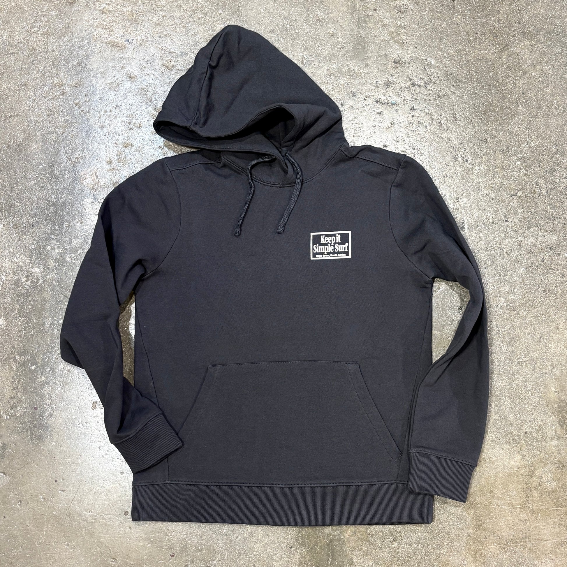 A grey pullover hoodie with a small white rectangular chest logo reading 'Keep It Simple Surf', laid flat on a textured concrete surface.