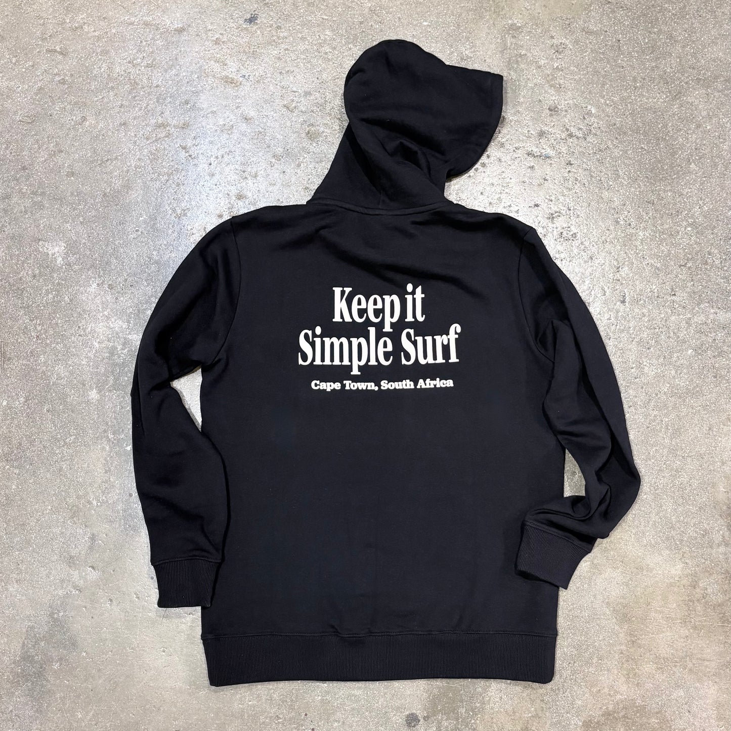Black hoodie with 'Keep it Simple Surf' text on a concrete surface