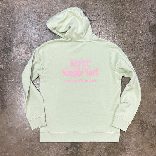 A light sage green hoodie with pink text reading 'Keep It Simple Surf' on the back, laid flat on a textured concrete floor.