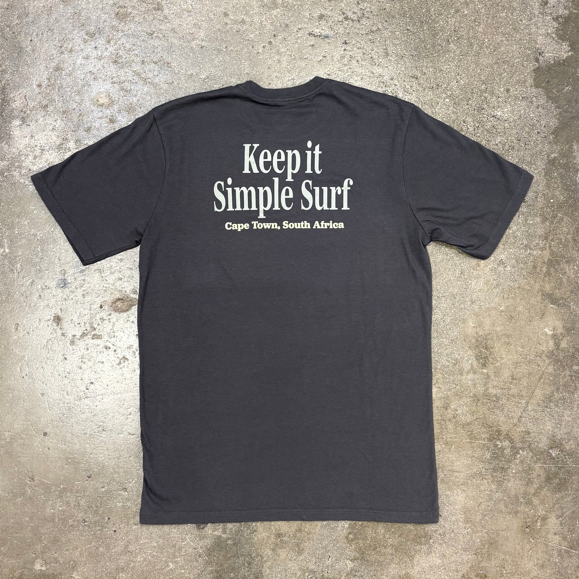 Grey t-shirt with 'Keep it Simple Surf' text on a concrete surface