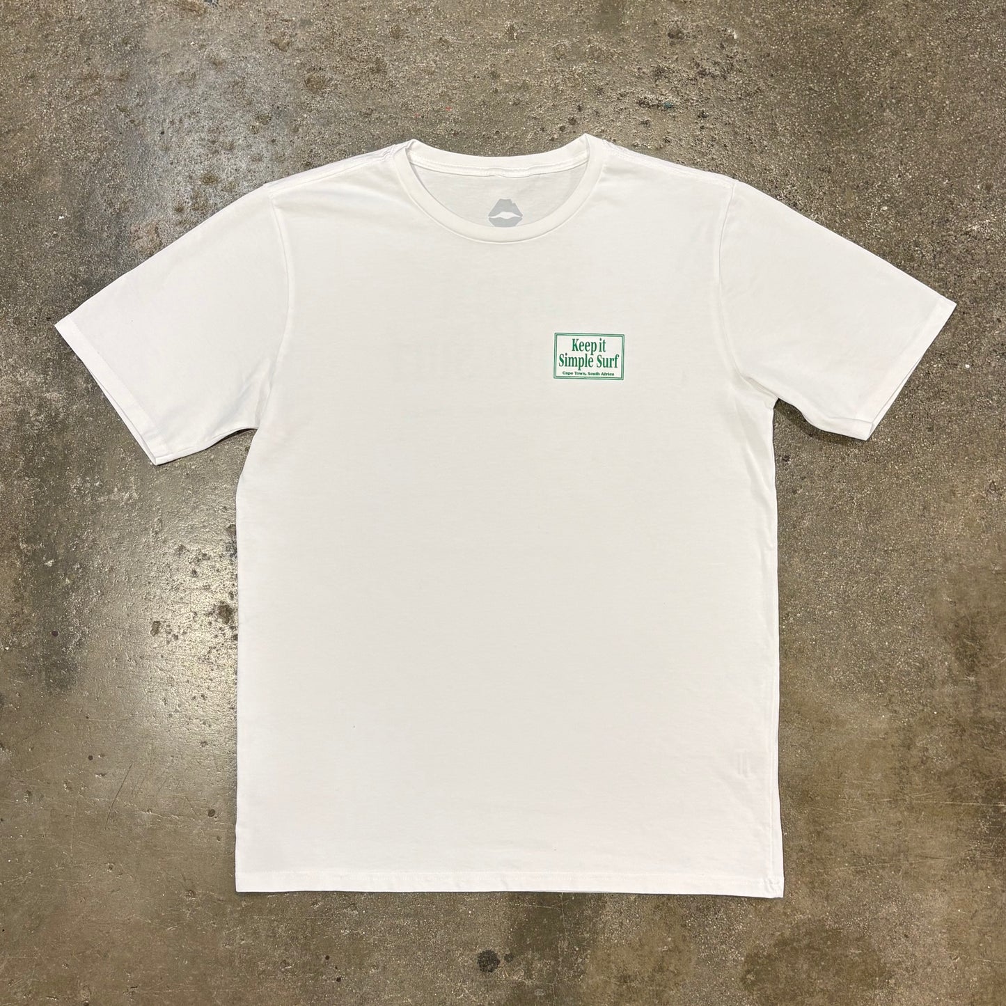 White t-shirt with a small green logo on a concrete surface