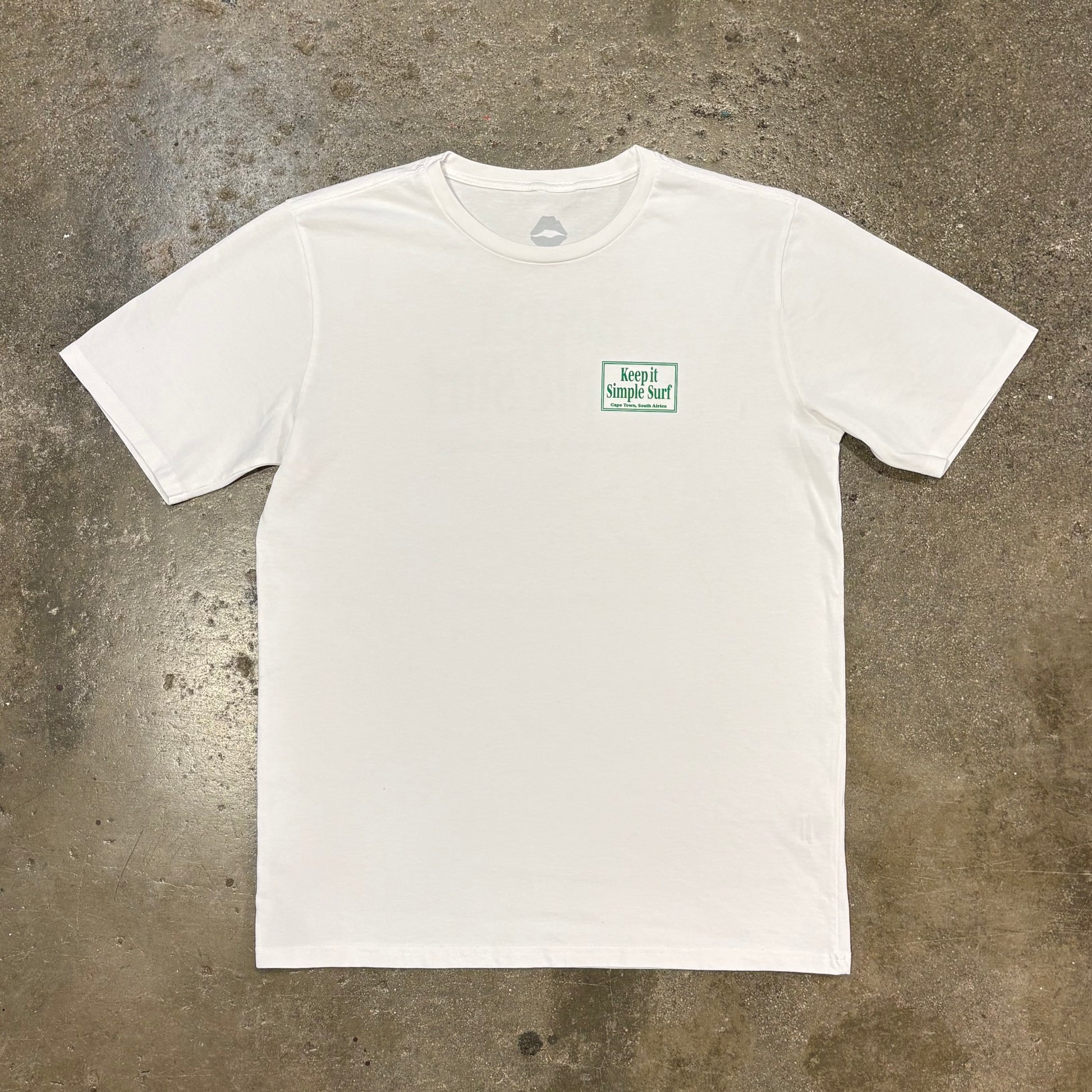 White t-shirt with a small green logo on a concrete surface