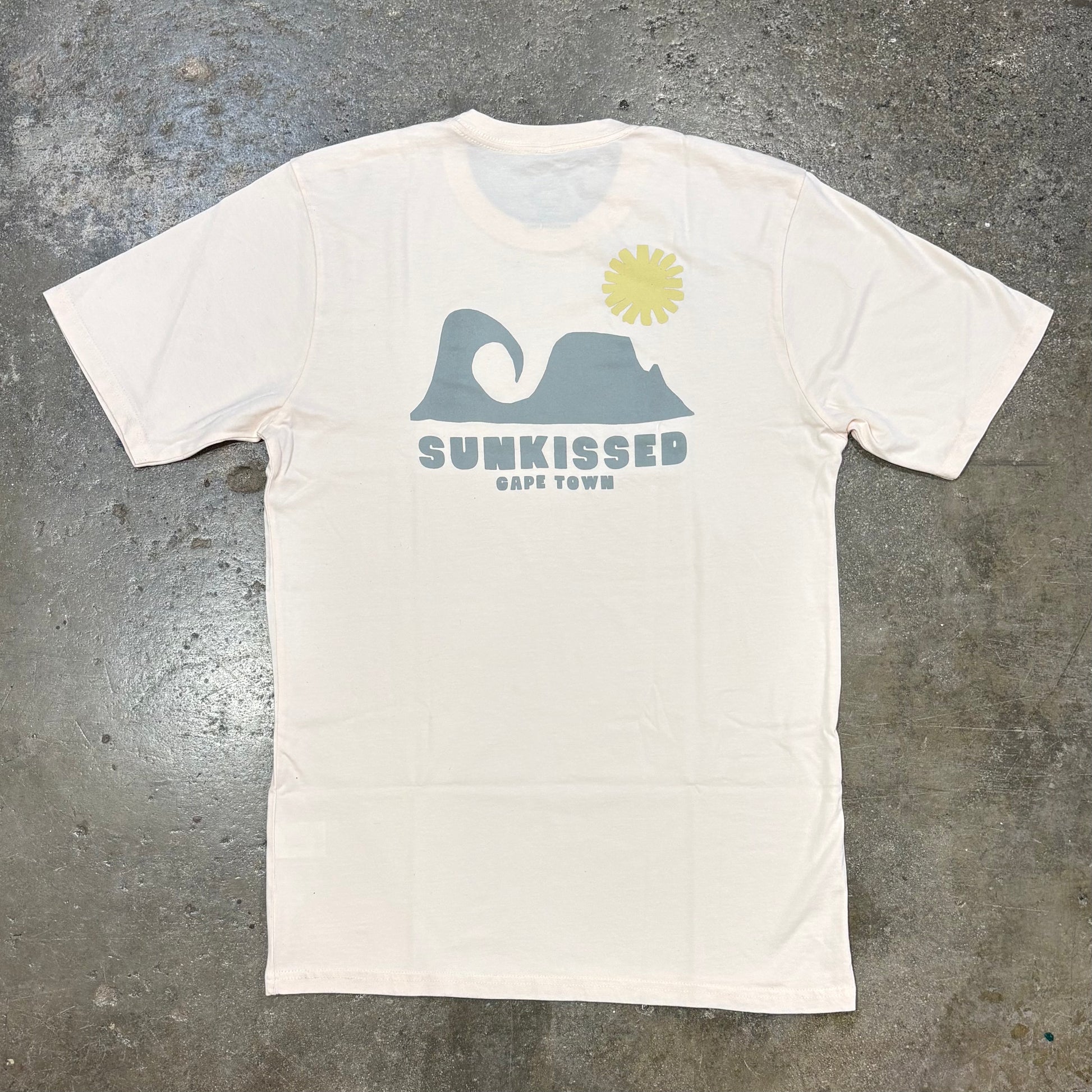 Dusty Pink t-shirt with grey graphic and 'Sunkissed Cape Town' text on a gray concrete surface