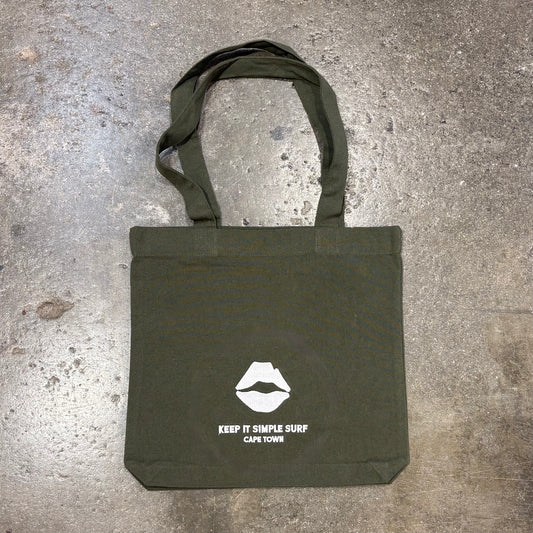 Green Kiss Surf Store  tote bag with white logo and text on a concrete surface