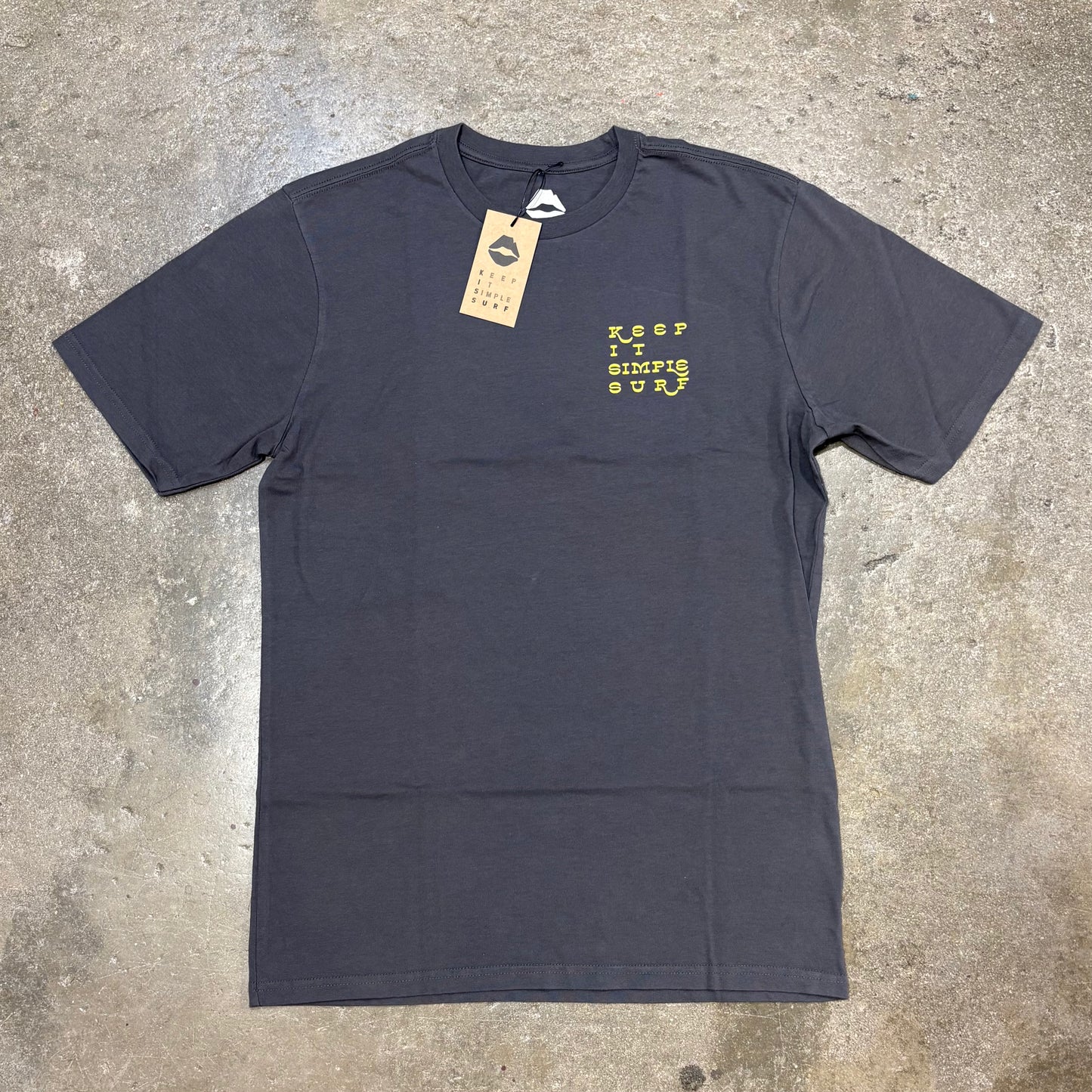 Dark gray Kiss t-shirt with yellow text on a concrete surface