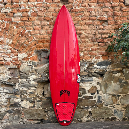 Red Mayhem surfboard with a logo against a stone wall background