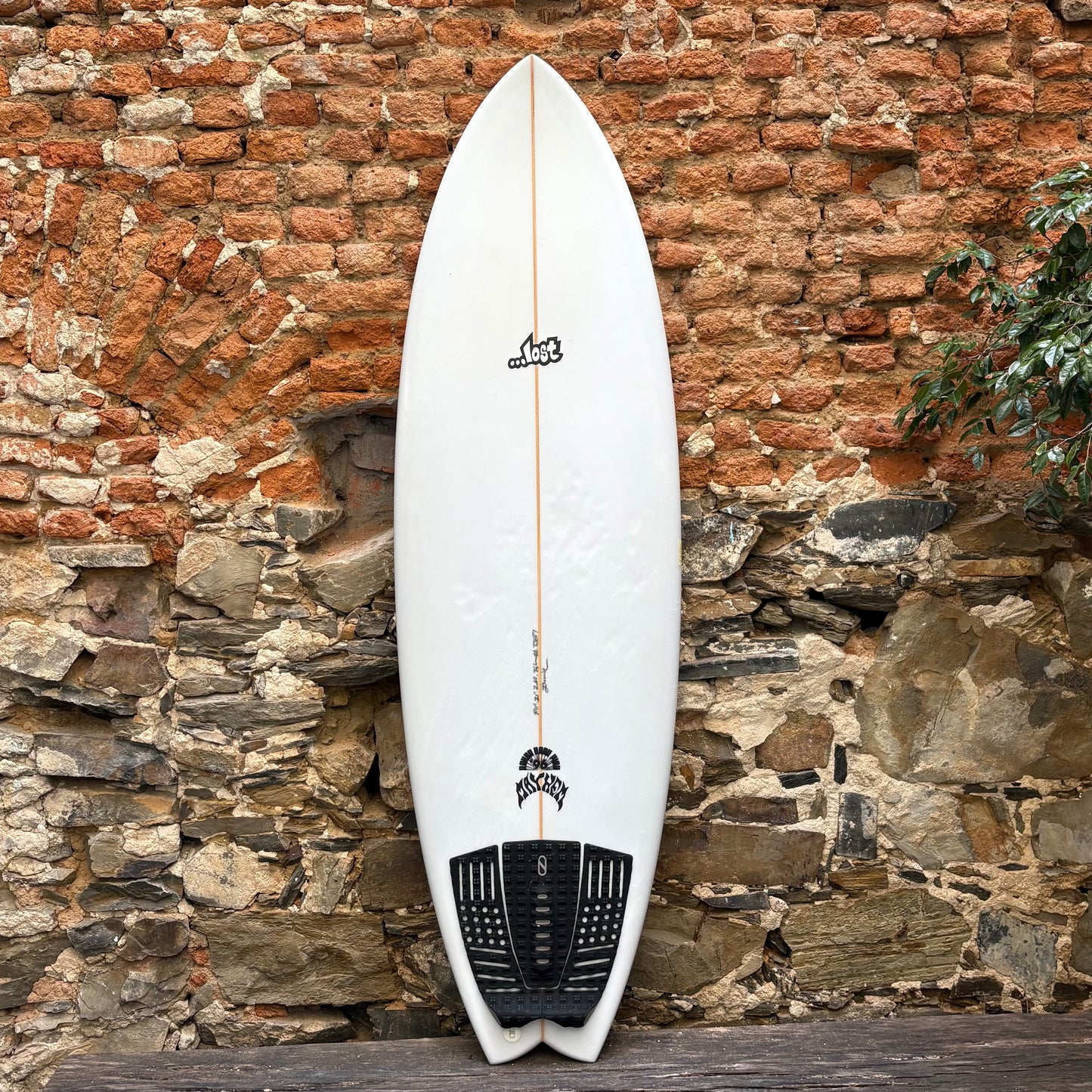 White surfboard with black logo against a stone wall