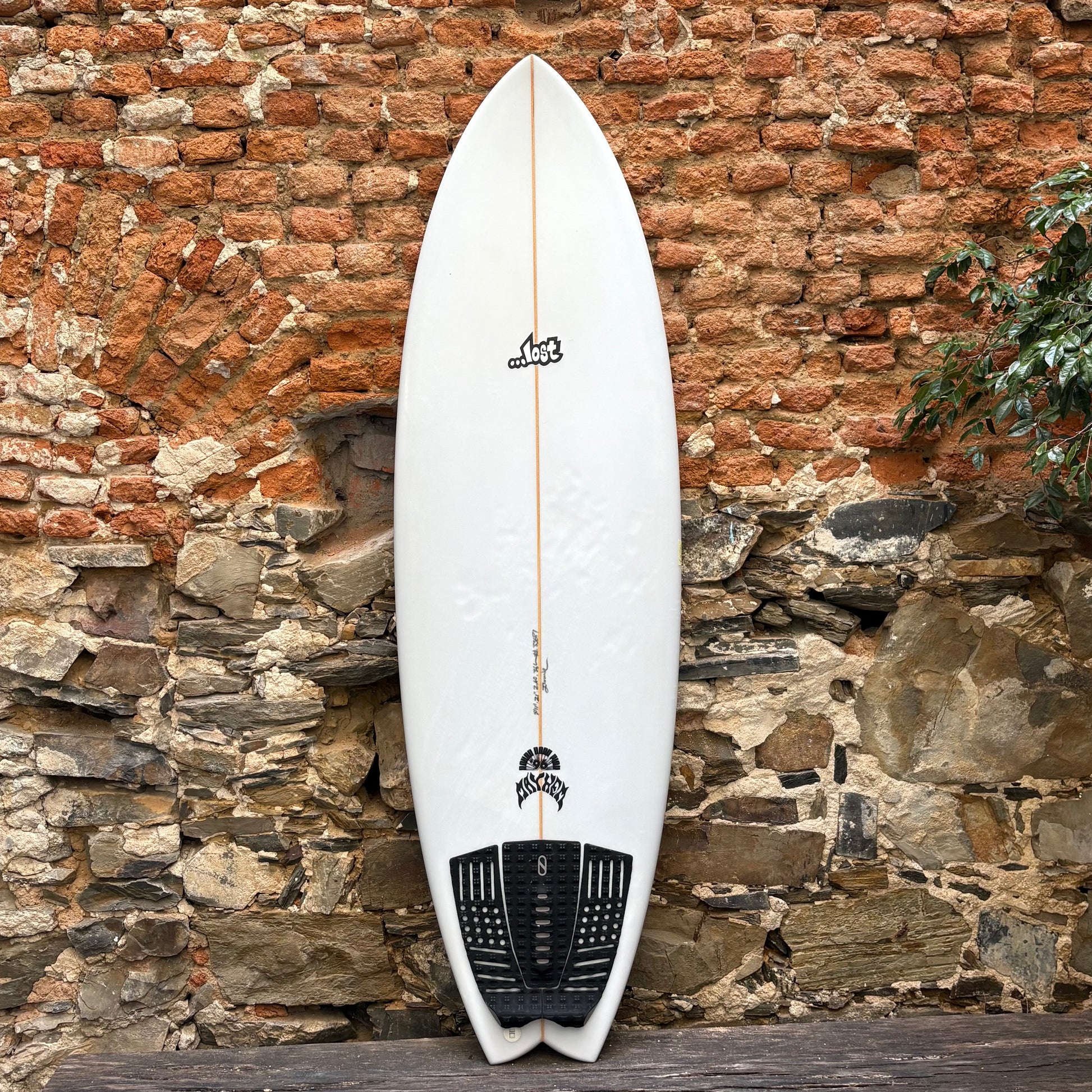 White surfboard with black logo against a stone wall