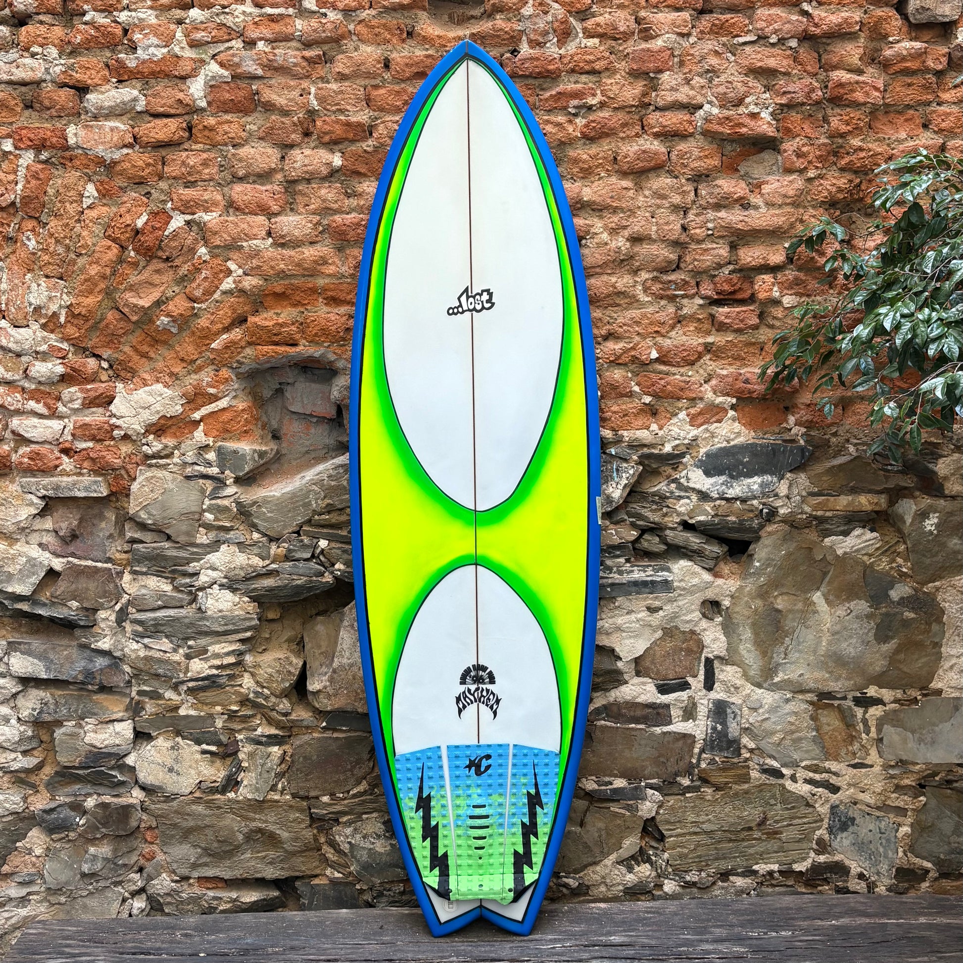Colorful surfboard with a white background against a stone wall.