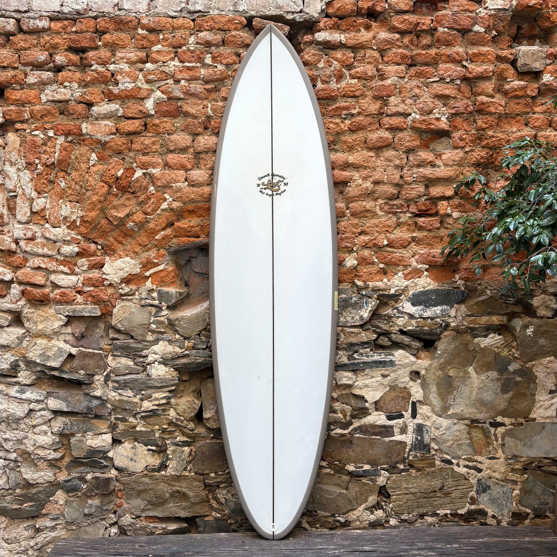White surfboard leaning against a rustic stone wall.