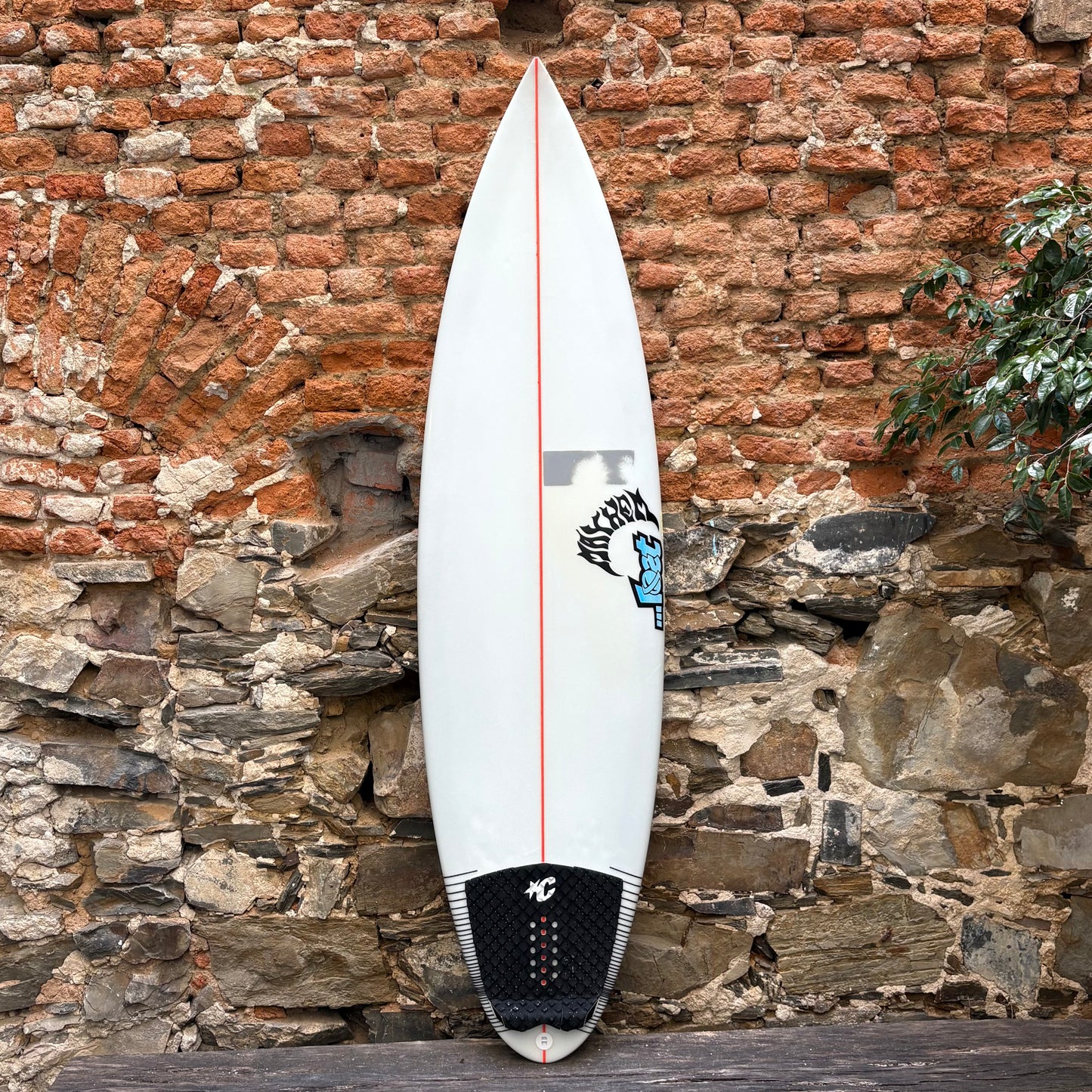 White surfboard with red accent against a rustic stone wall