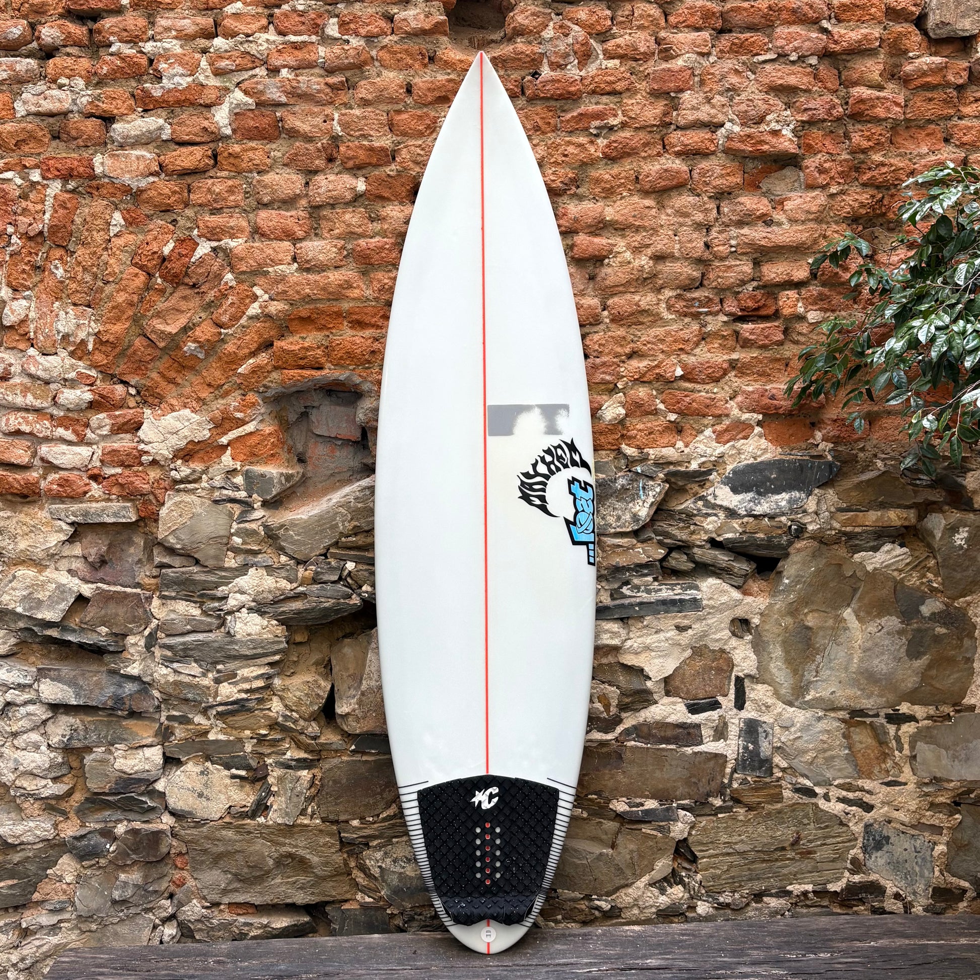 White surfboard with red accent against a rustic stone wall