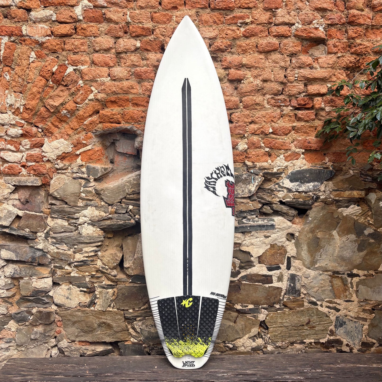 White surfboard with black and yellow design against a stone wall.