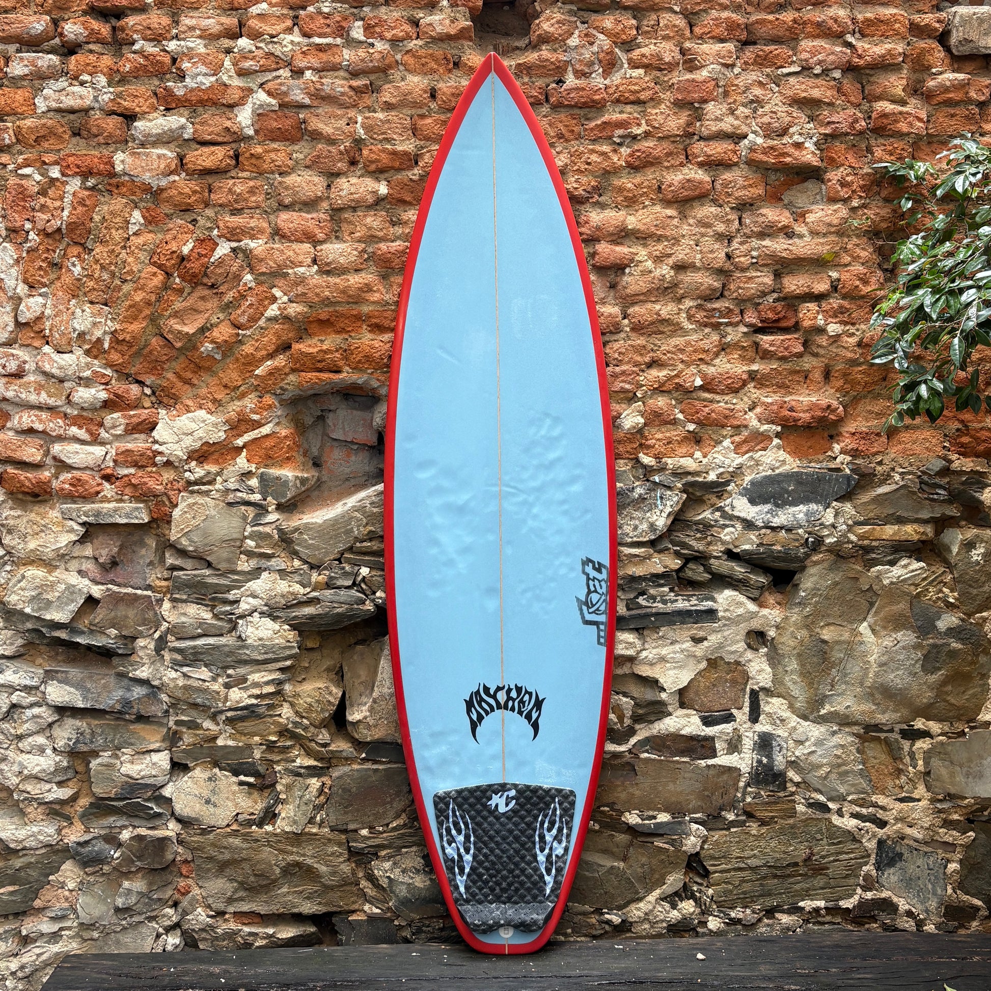 Blue surfboard with red edges leaning against a stone wall.