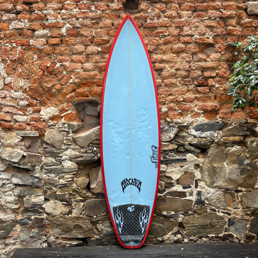 Blue surfboard with red edges leaning against a stone wall.