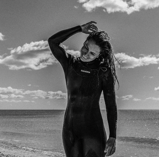 Person wearing a wetsuit with 'Manera' branding on a beach