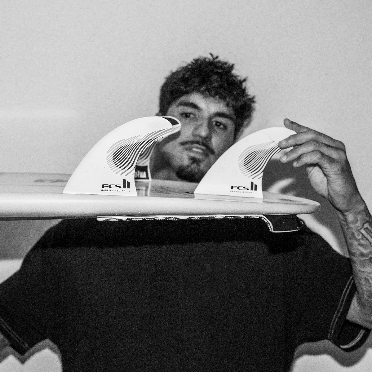 Gabriel Medina holding a surfboard with FCS fins, black and white photo