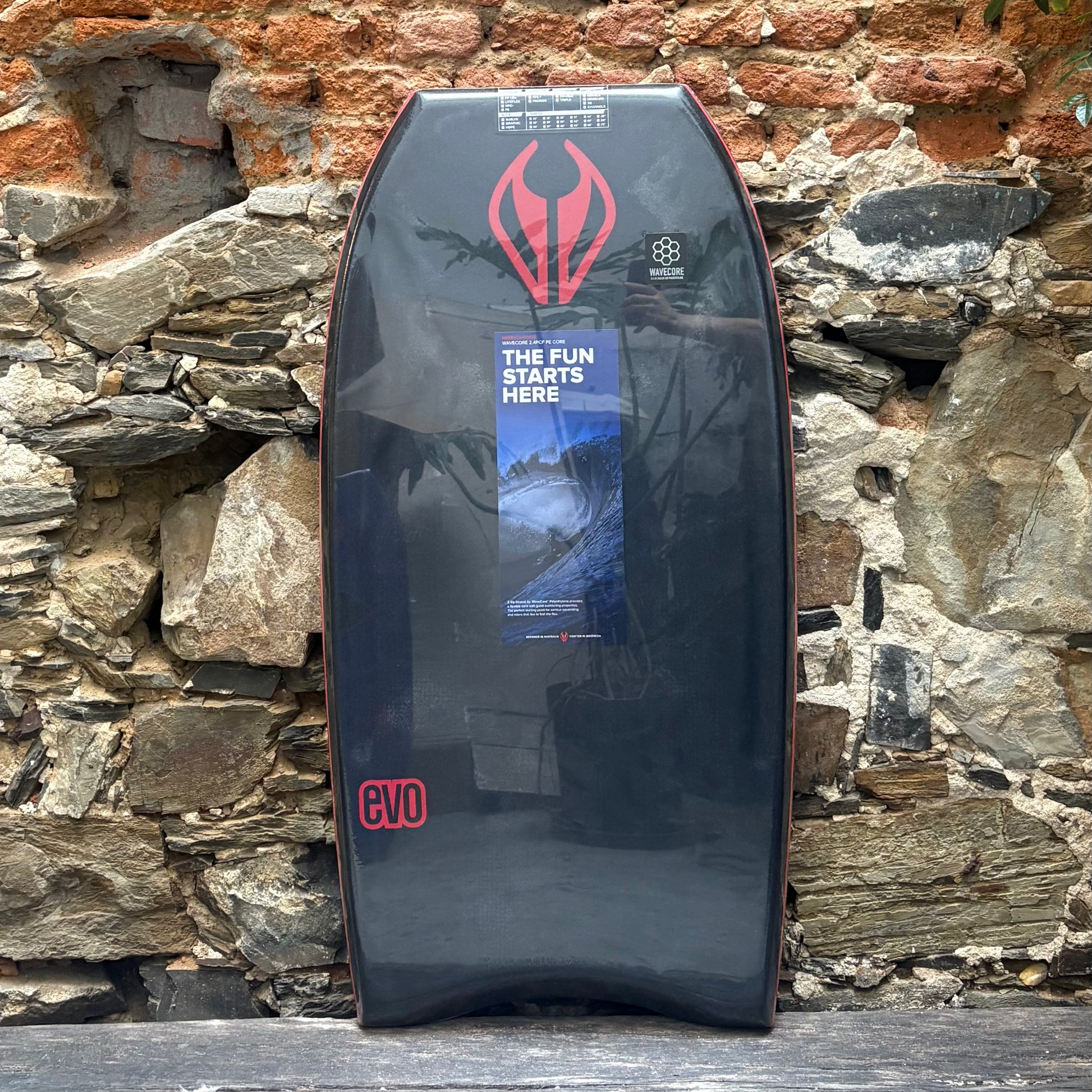 Bodyboard with red logo against a stone wall