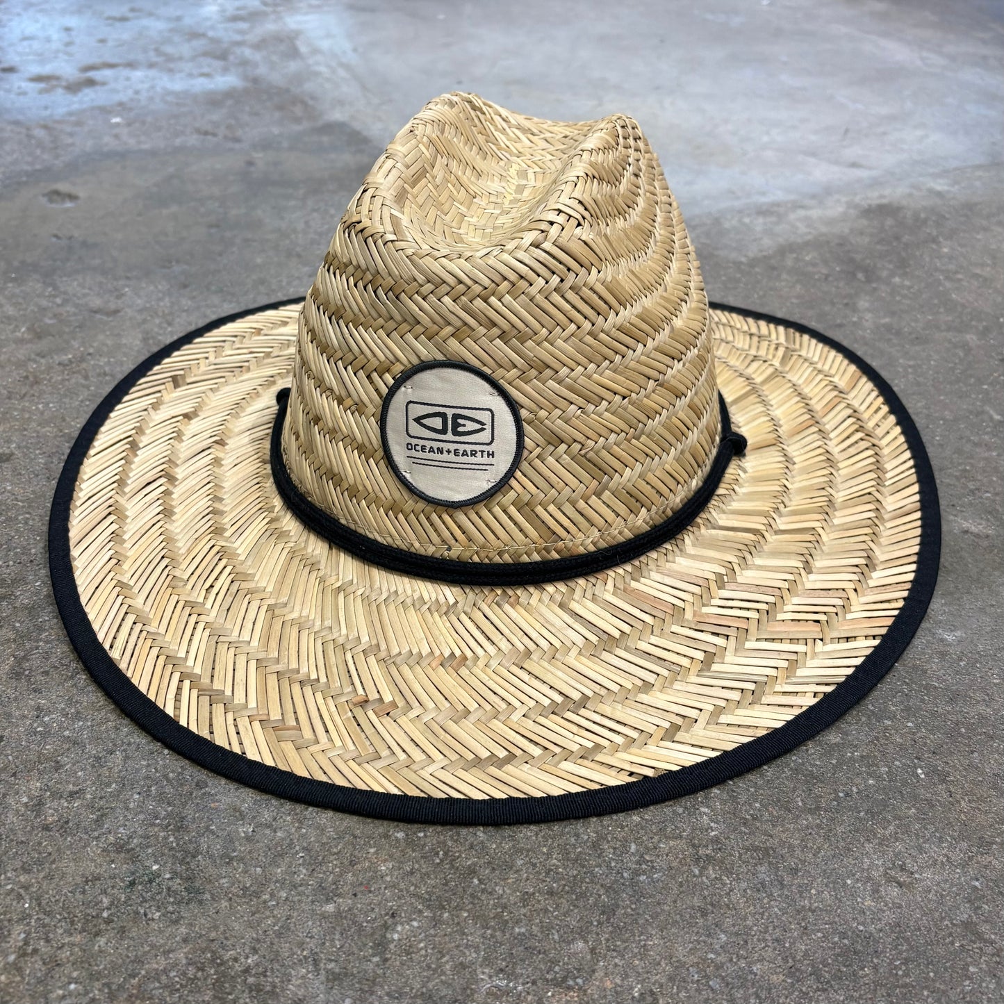 Straw hat with a black band and logo on a concrete surface