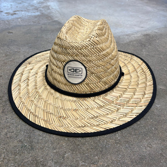 Straw hat with a black band and logo on a concrete surface