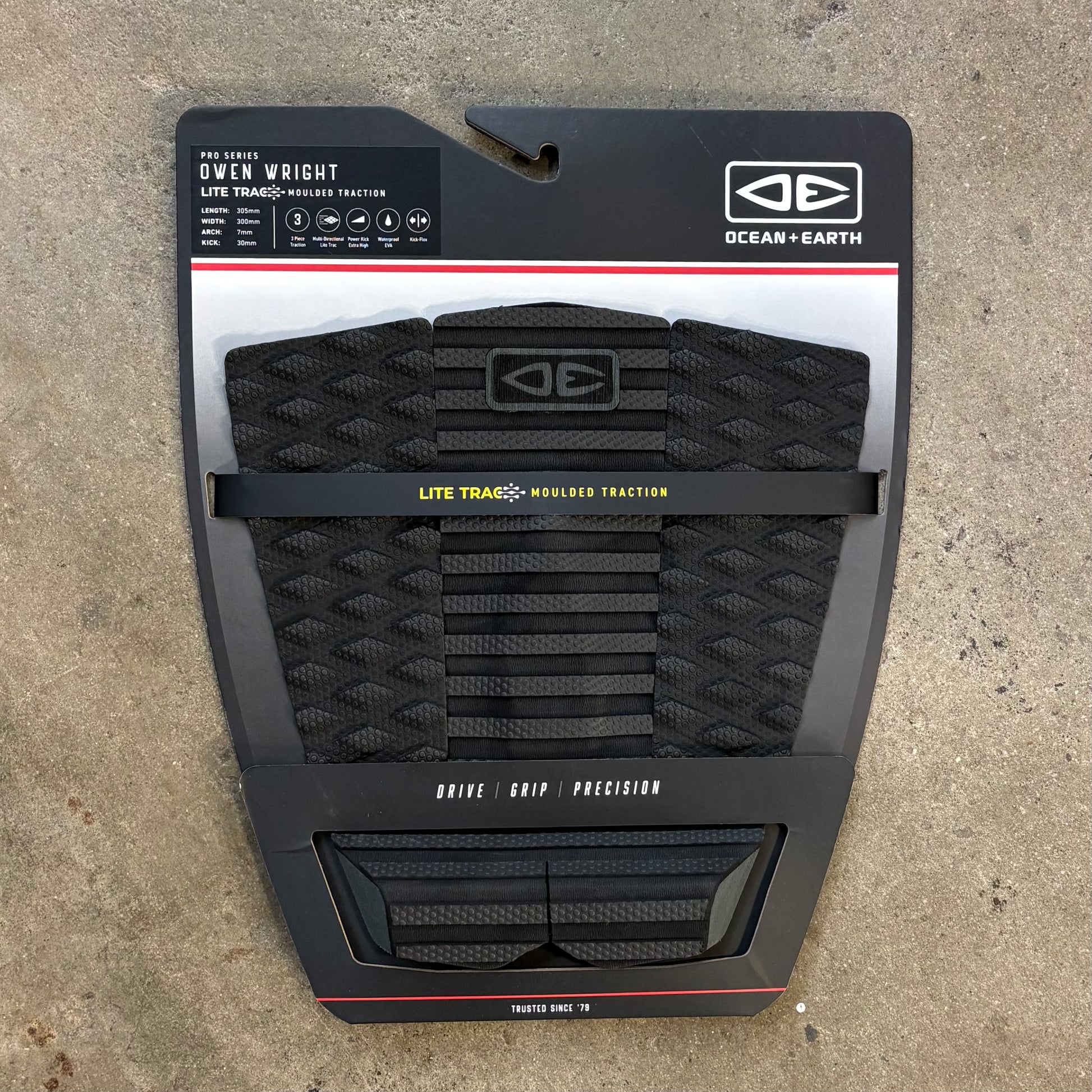 Packaged black surfboard traction pad with branding on a concrete surface