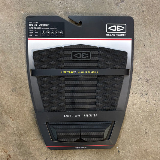 Packaged black surfboard traction pad with branding on a concrete surface
