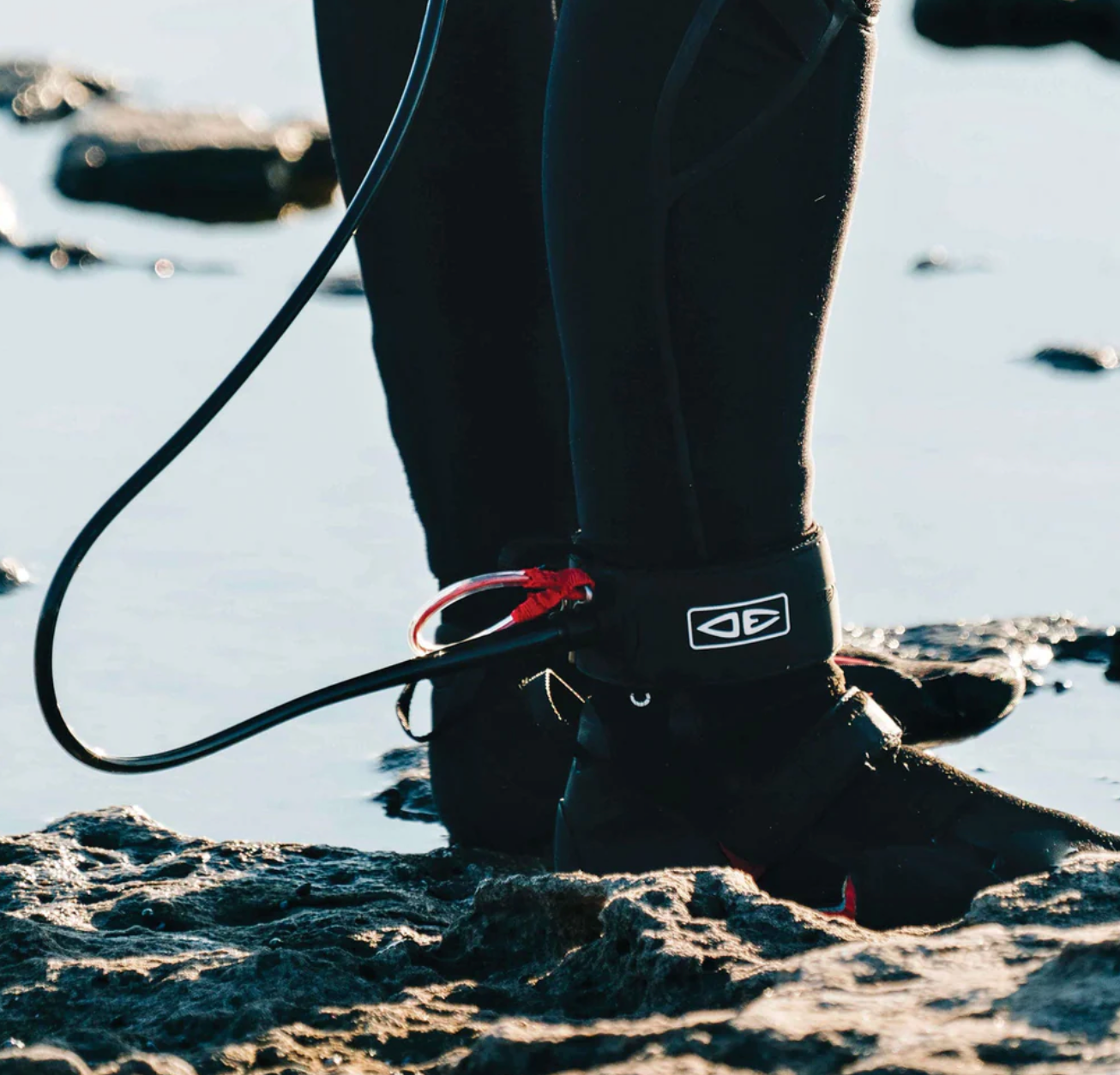 Person wearing a wetsuit with a leash on a beach