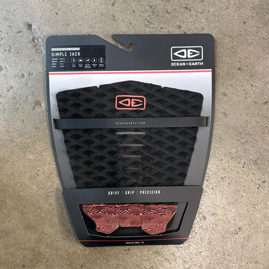 Black and red surfboard leash pad with Ocean and Earth branding on a concrete surface