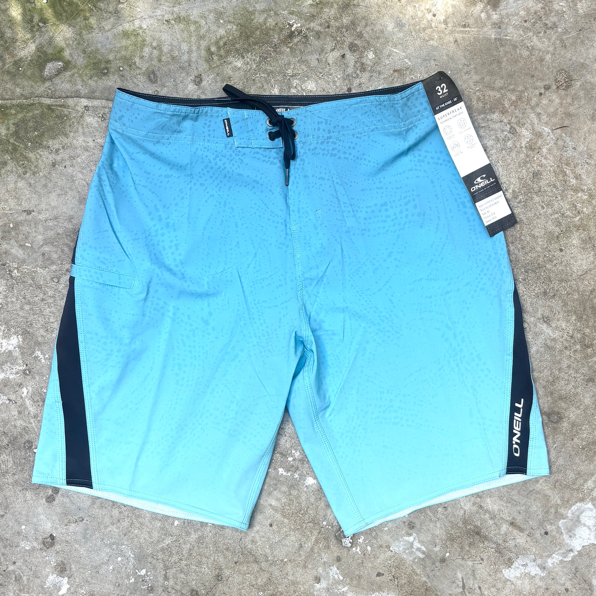 Light blue O'Neill board shorts with black side panels and a black drawstring, laid flat on a concrete surface with a product tag attached.