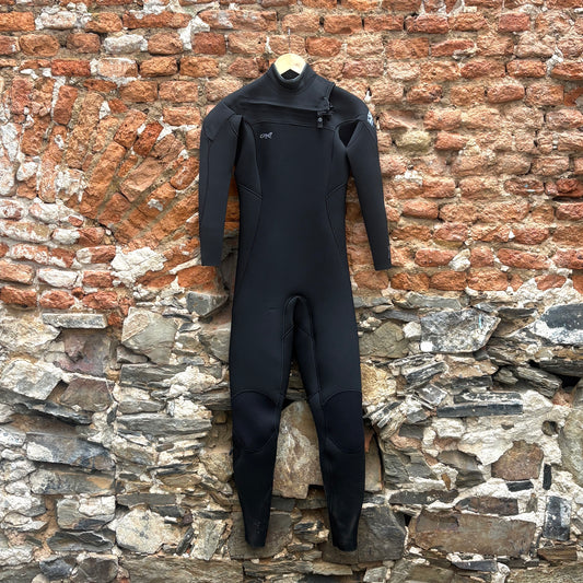 A black full-body wetsuit hangs from a wooden hanger against a rustic brick and stone wall.