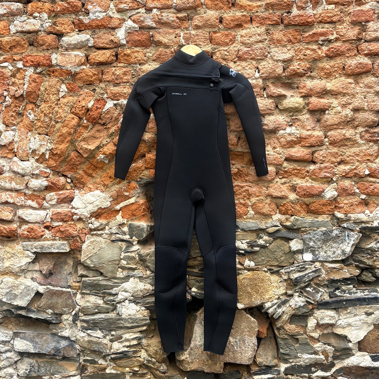 Front view of O'Neill Youth Epic 4/3mm+ Chest Zip - Black in front of a rustic stone wall