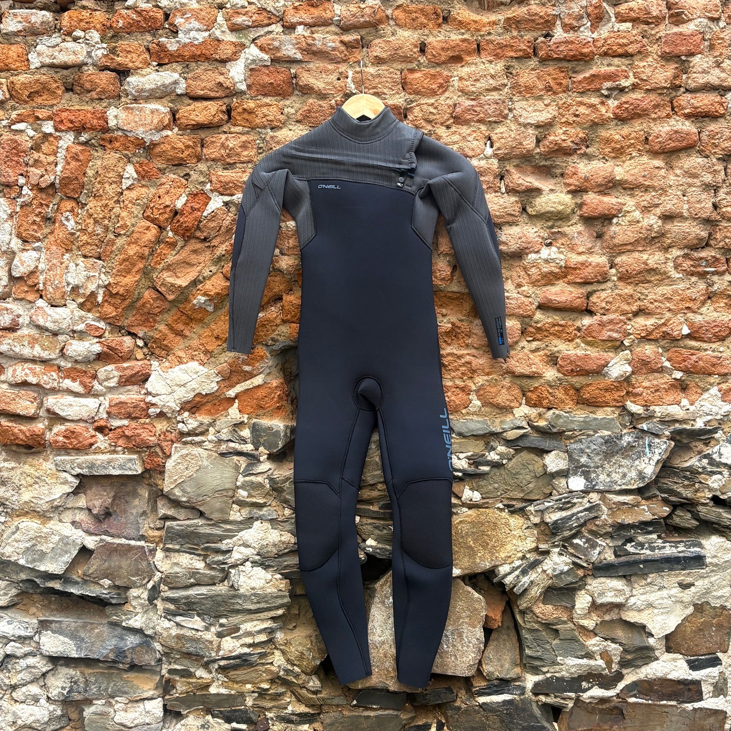 Front view of O'Neill Youth Hyperfreak 4/3mm+ Chest Zip Wetsuit - Black/Tempered Steel in front of rustic stone wall