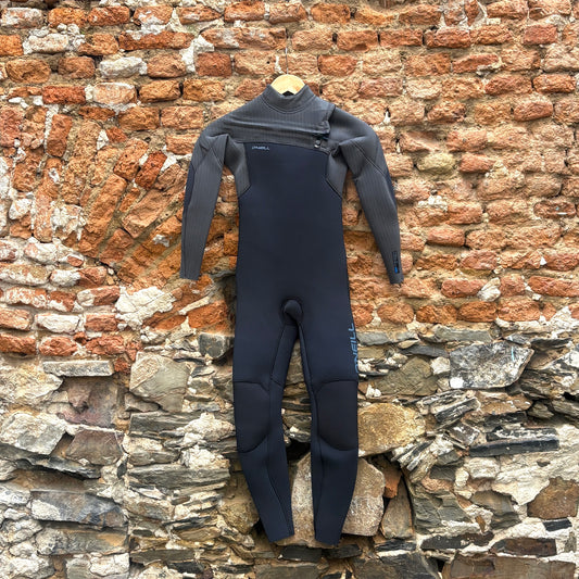 Front view of O'Neill Youth Hyperfreak 4/3mm+ Chest Zip Wetsuit - Black/Tempered Steel in front of rustic stone wall