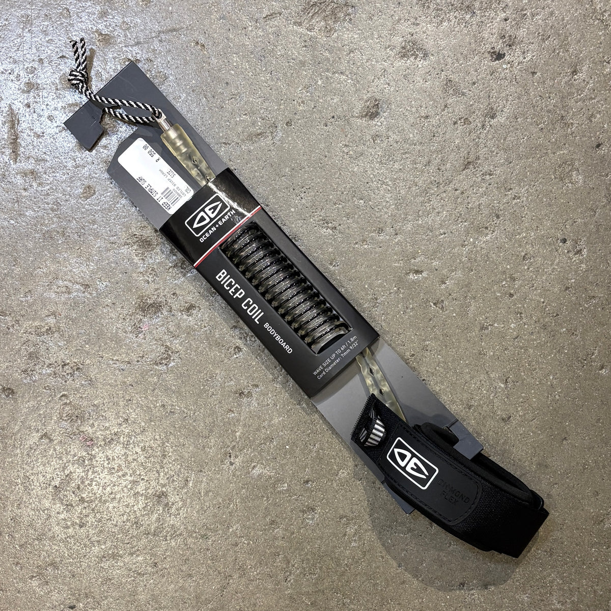 A packaged set of black bowfied coil arrows with a black and white striped nock, shown in its retail packaging on a textured concrete floor. The packaging features a black cardboard sleeve with the brand logo and text 'BOWFIED COIL ARROWS'.