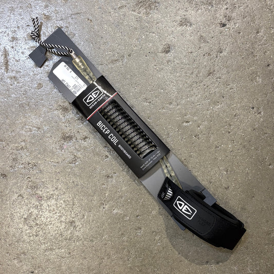A packaged set of black bowfied coil arrows with a black and white striped nock, shown in its retail packaging on a textured concrete floor. The packaging features a black cardboard sleeve with the brand logo and text 'BOWFIED COIL ARROWS'.