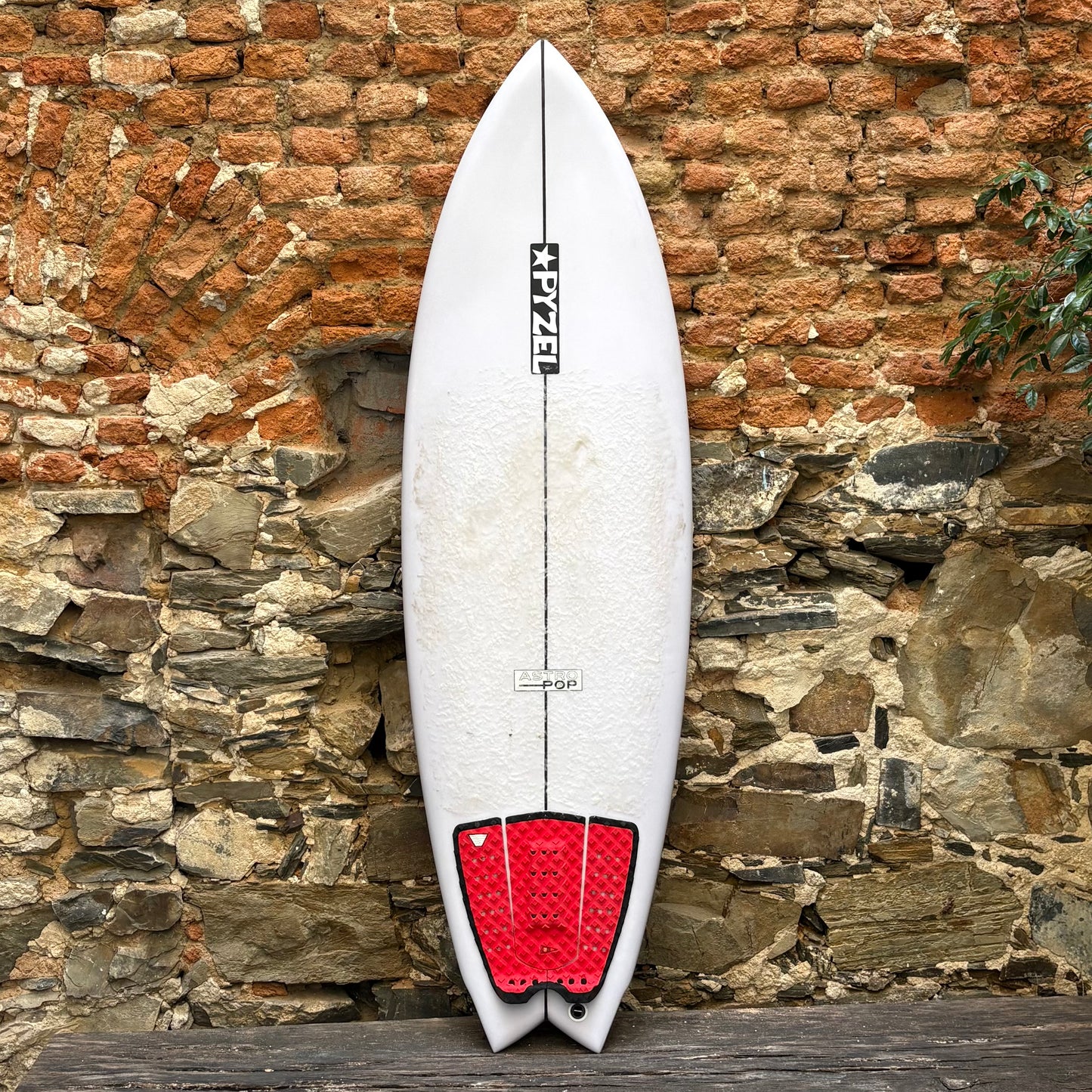 White surfboard with red tail fin against a stone wall